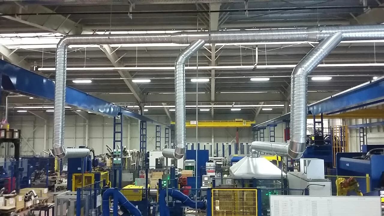 Üretim holünde çatı makaslarına asılmış spiral galvaniz kanal hattı ve tezgâhlara inen emiş kolları.